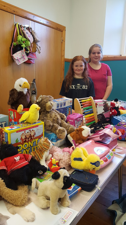 table with second hand toys with two smiling girls at coffee morning