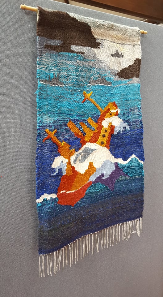 finished community tapestry shows a large orange boat in the foreground with the color palette becoming more muted into the horizon